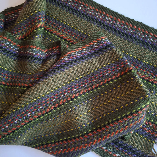A close-up of a woven  scarf, featuring a multicolor striped pattern with olive green,  purple, orange, yellow, and white threads.